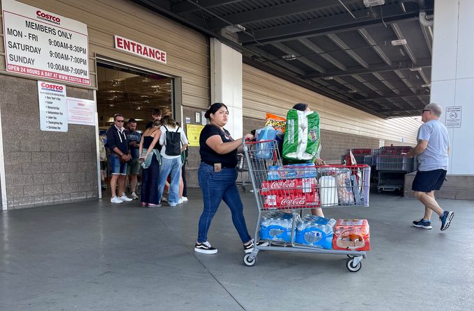 Woman pushes cart full of bulk items outside the entrance of a Costco store