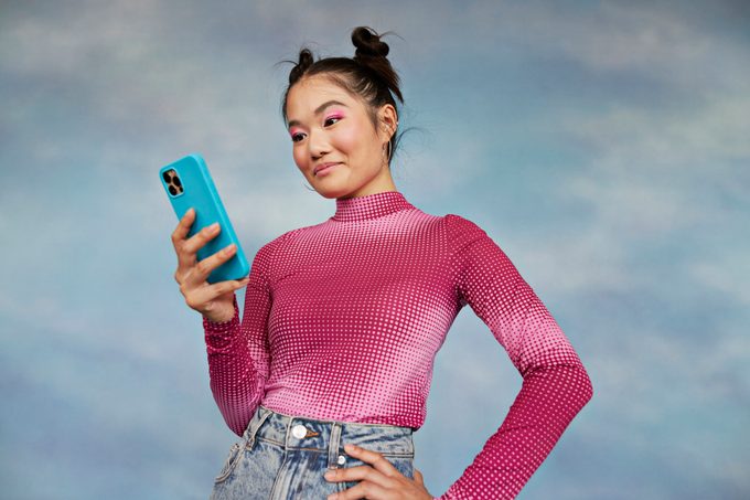 Teenage girl using mobile phone while standing against blue background