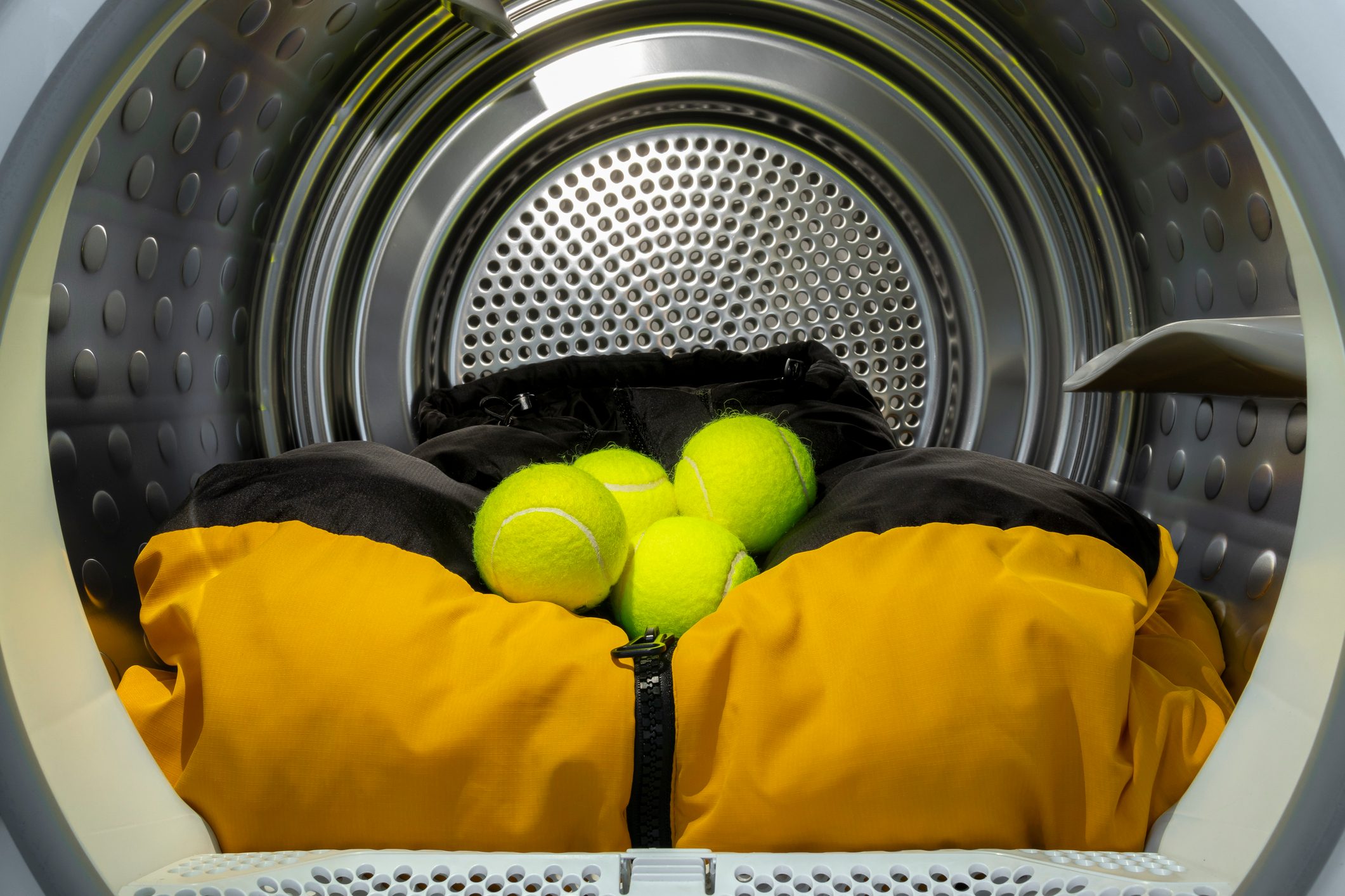 Multiple tennis balls with clothes in tumble dryer drum