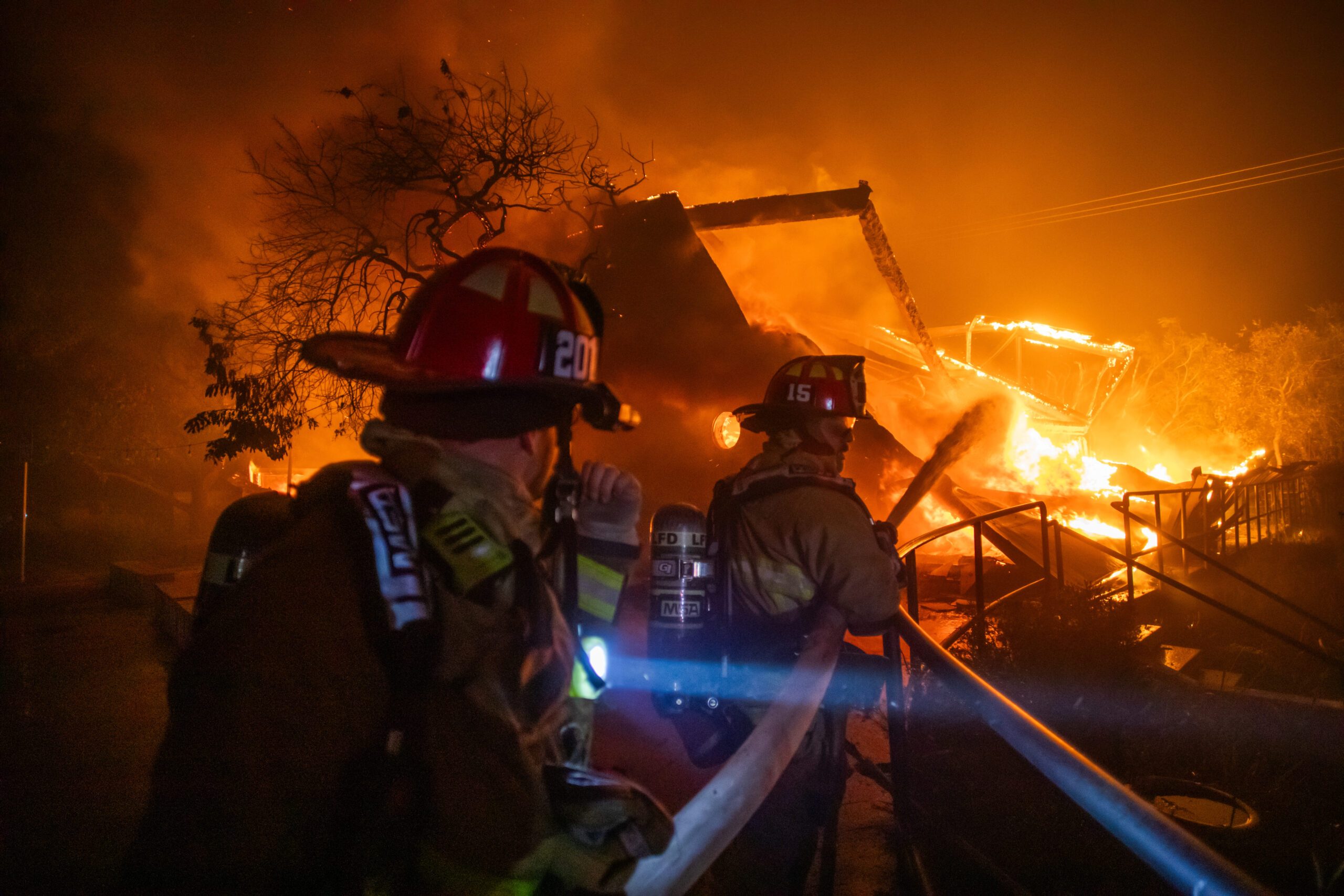 Firefighters in Los Angeles shine flashlights on a burning structure
