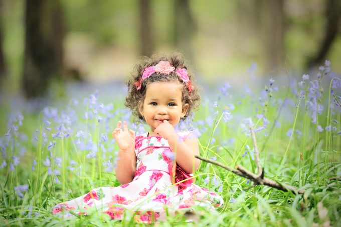 Baby wearing a pink floral dress surrounded by blue flowers in a meadow