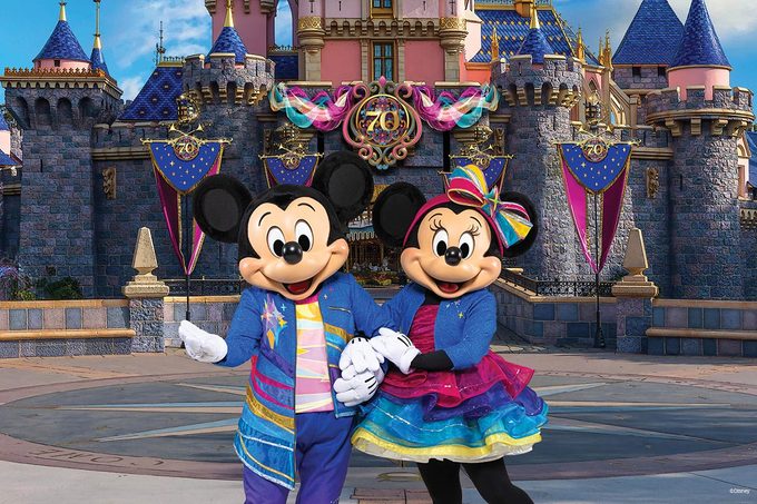 Mickey and Minnie Mouse in colorful outfits pose in front of Sleeping Beauty's castle at Disneyland