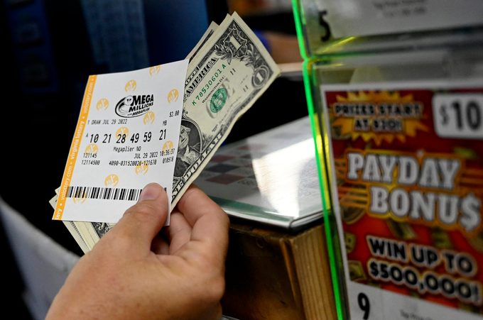 Hand holds a mega millions lottery ticket with dollar bills at a cash register