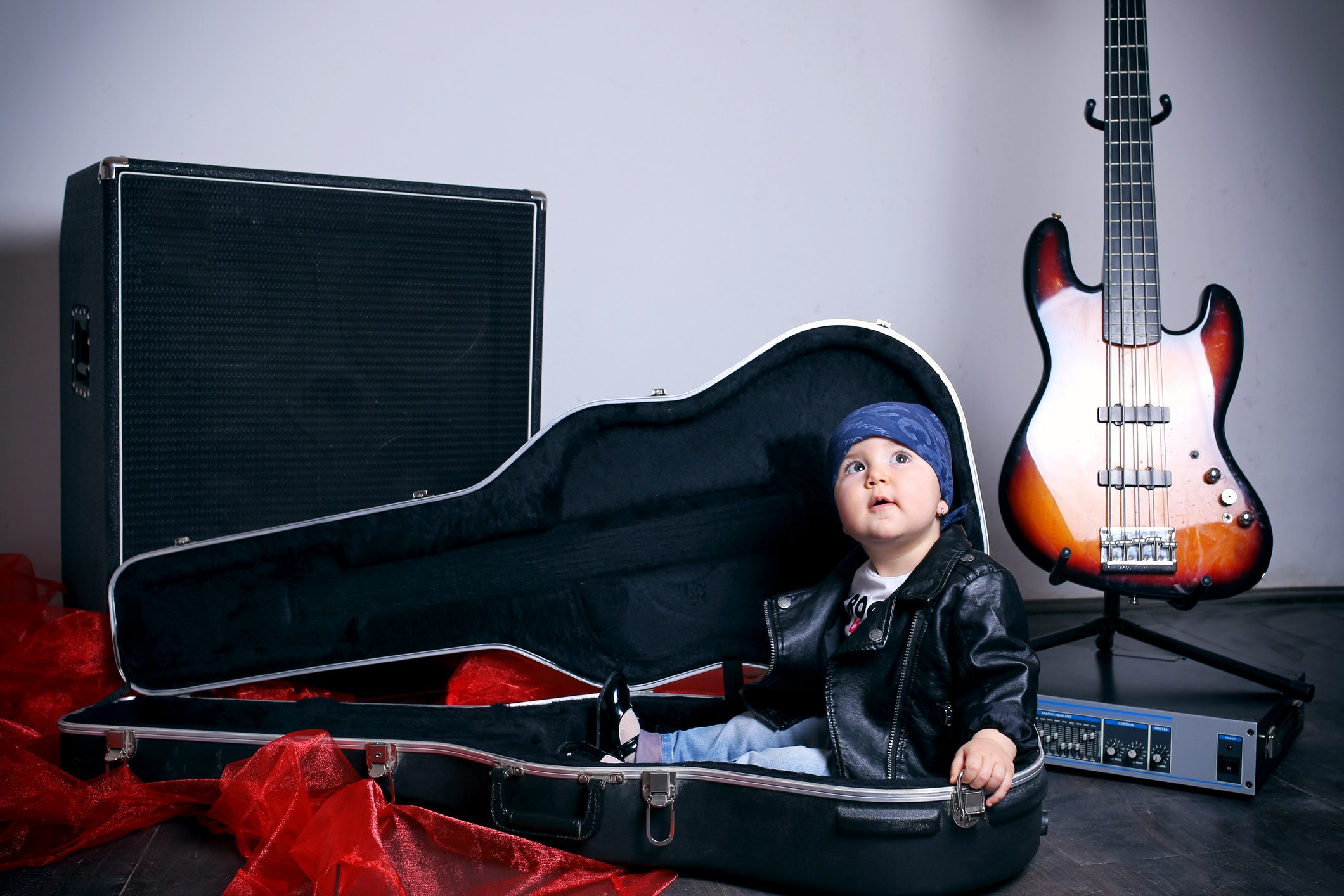 Cute little rocker-baby girl sitting in a guitar case with an electric guitar to the right