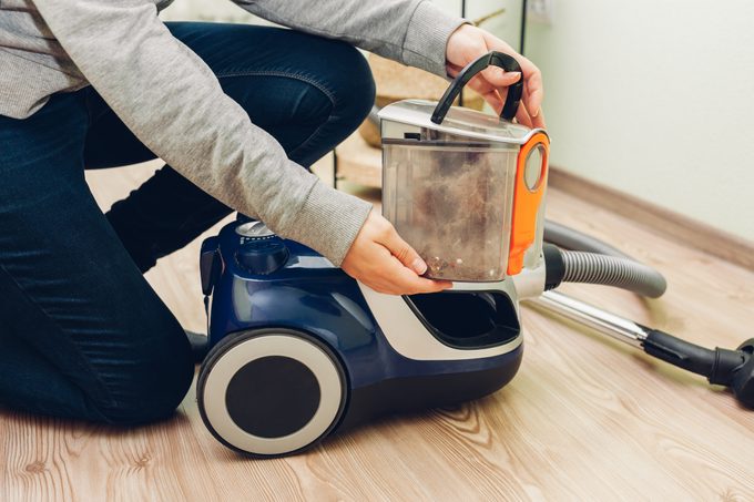 Woman takes container with dust filter out of canister vacuum cleaner at home