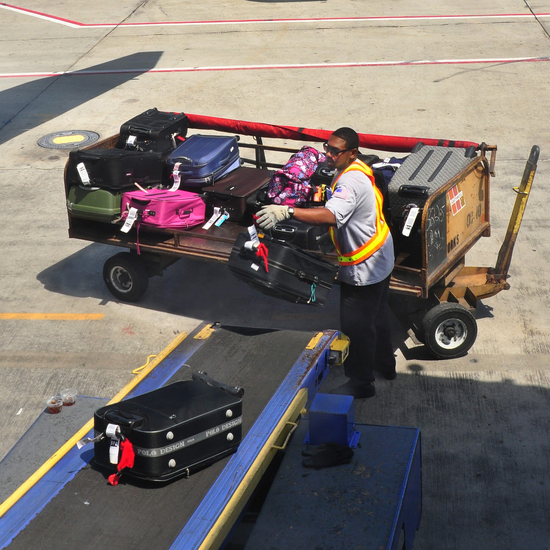 Baggage handler loading suitcases onto a conveyor belt leading to a plane