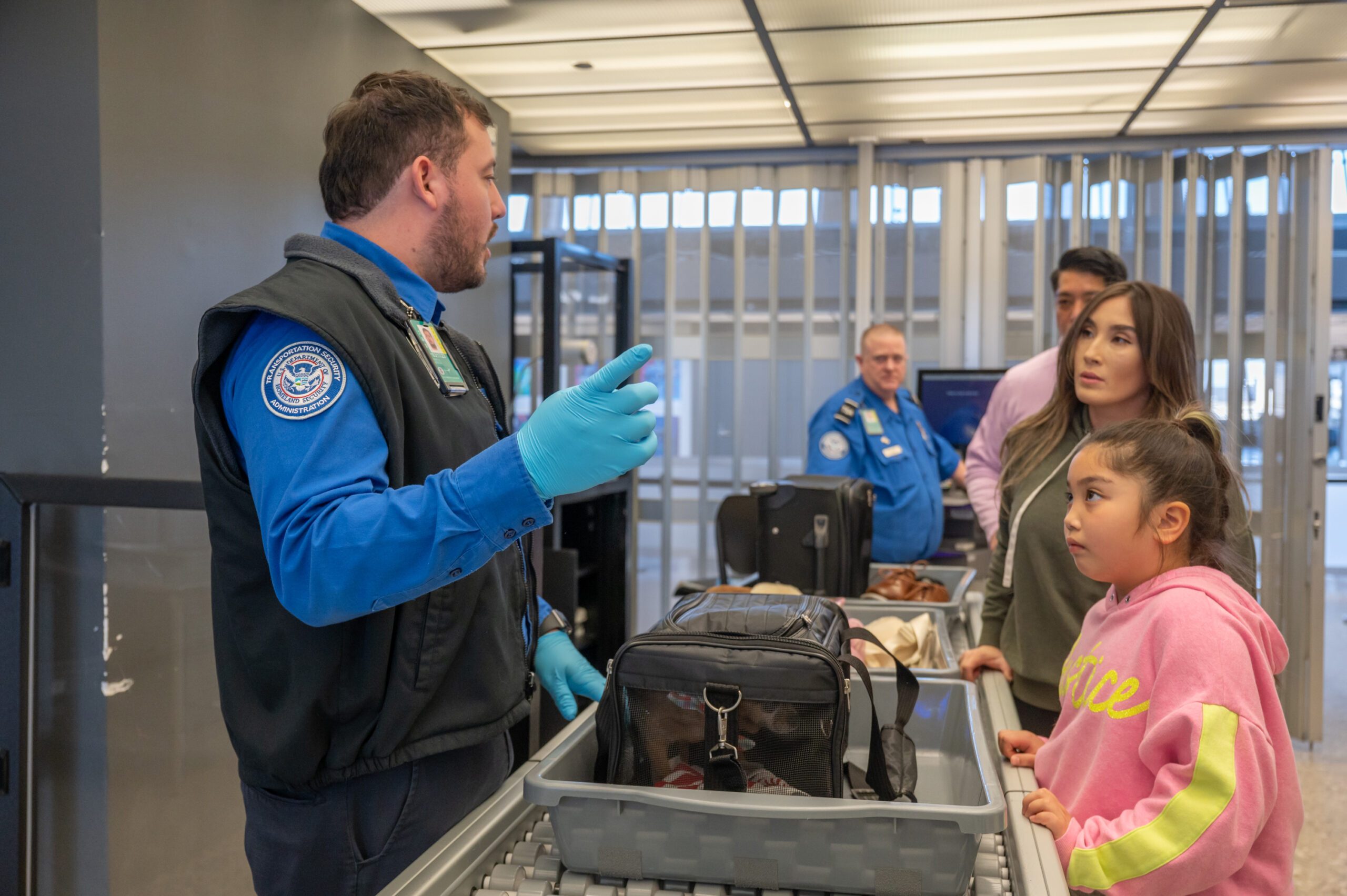 TSA agent talks to airline passengers across the baggage scanner