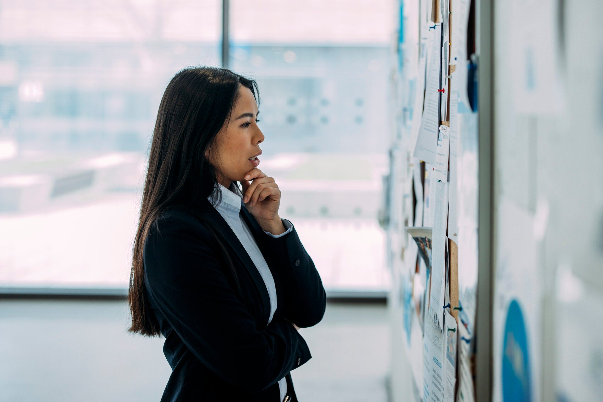 Thoughtful businesswoman examining bulletin board at office