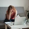Worried woman looking at forms and receipts sitting at laptop