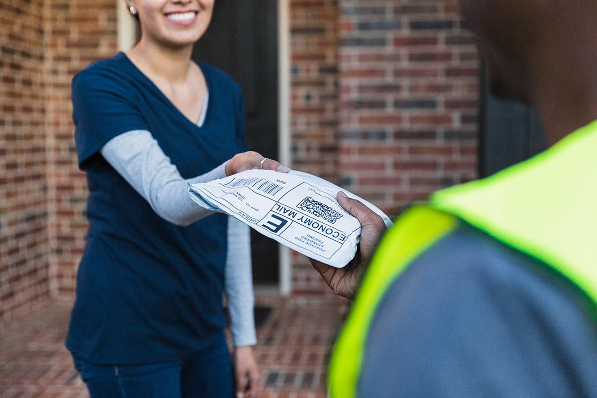 Woman smiles while recieving package from delivery person