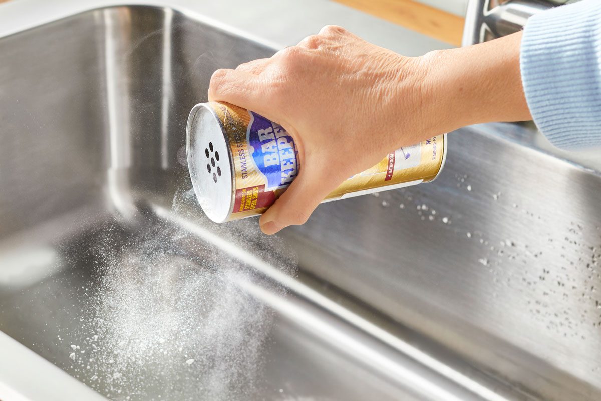 Hand spreading bar keeper's friend in a stainless steel sink