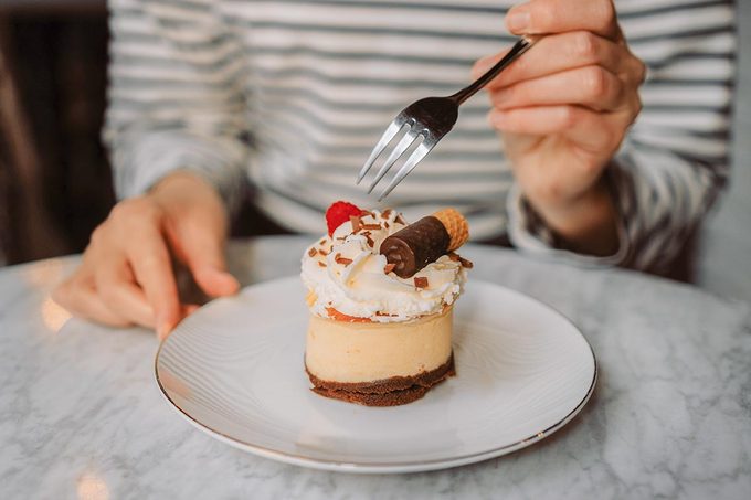 A close-up of a woman's hand holding a fork, about to slice into a dessert.