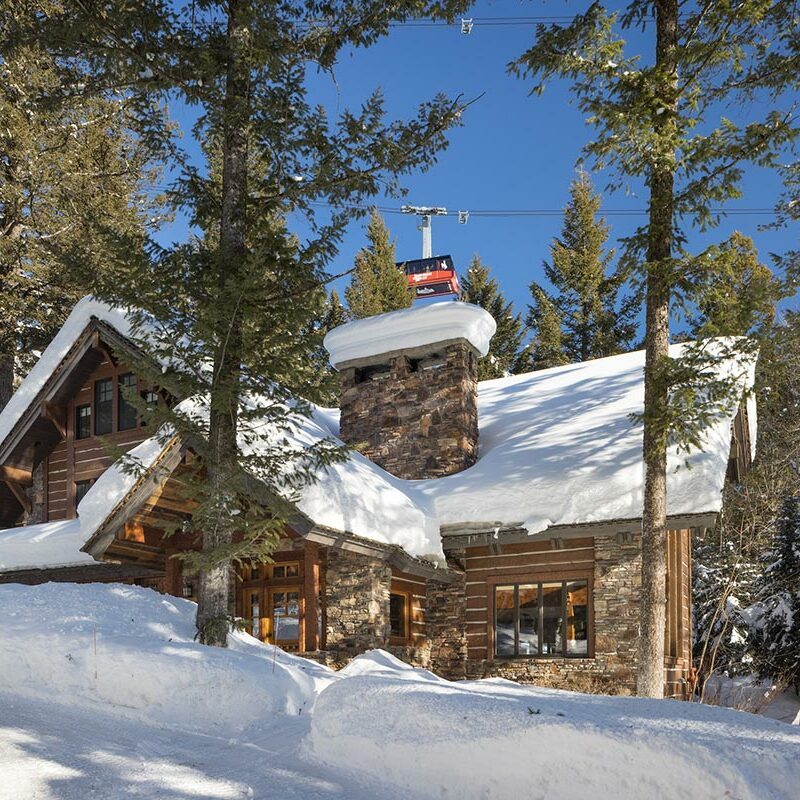 Stone cottage in a pine forest with snow drifts and a cable car in the background