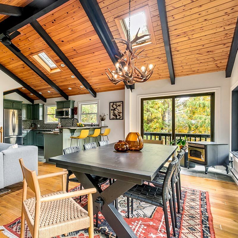 Living and dining room with vaulted ceiling, antler chandelier, and a view of a forest outside