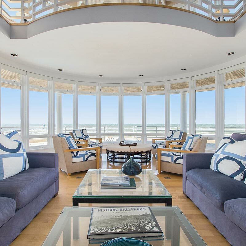 Wide shot of a light-filled living room with blue couches and windows looking out to a lake horizon
