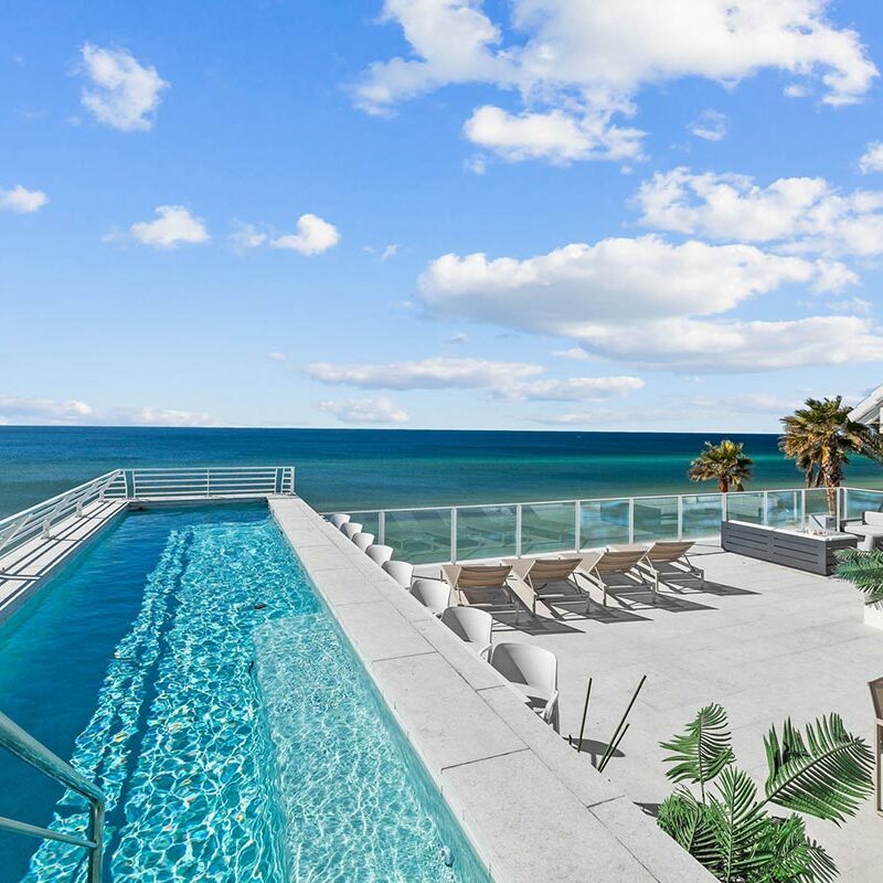 Long pool and lounging area overlooking a teal ocean under a blue sky
