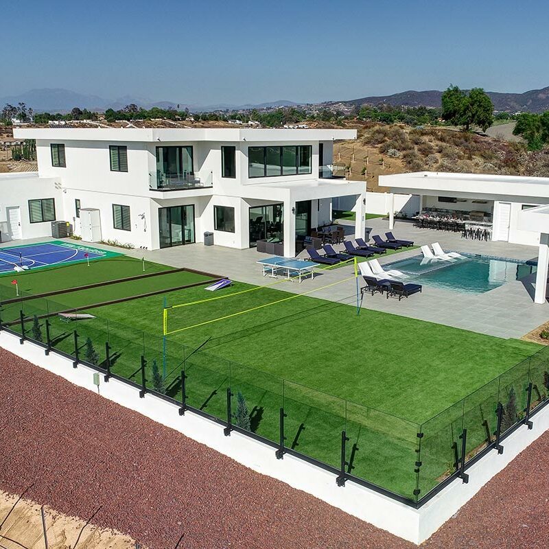 Aerial view of a house with astroturf yard, pool, basketball court, and patio area