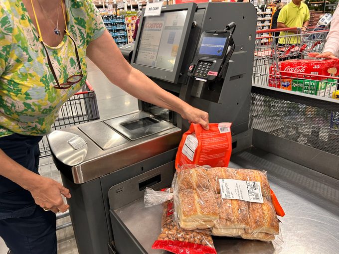 Woman using self checkout in Costco store purchasing bakery bread