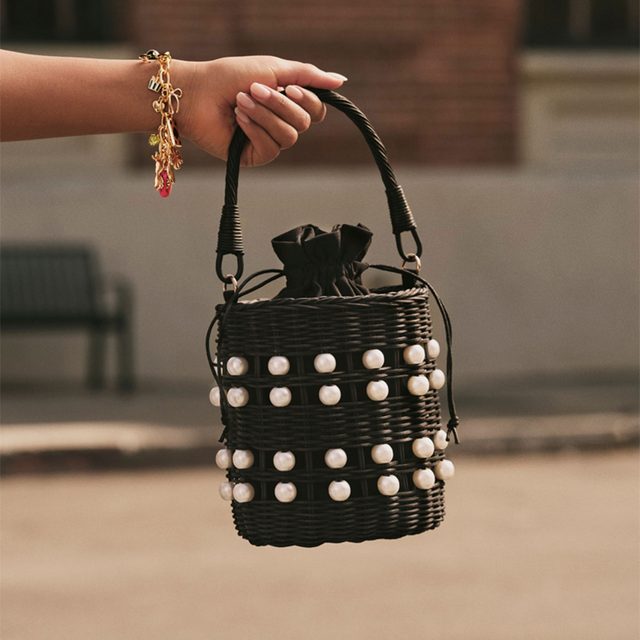 Hand holding a black wicker purse with white polka dots